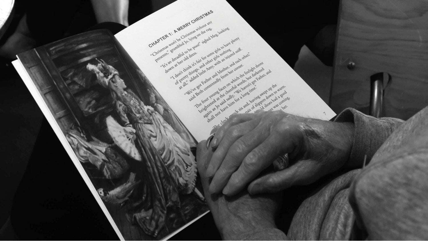 A close up looking downward on a person reading Little Women. The book is open on their lap and their hands are crossed over and resting on the book.